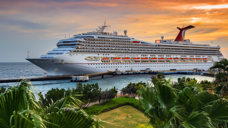 Carnival Conquest docked at Port Willemstad at sunset with lush foliage in foreground