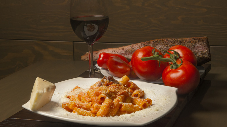 A plate of rigatoni all'amatriciana next to tomatoes and chiles and a glass of wine