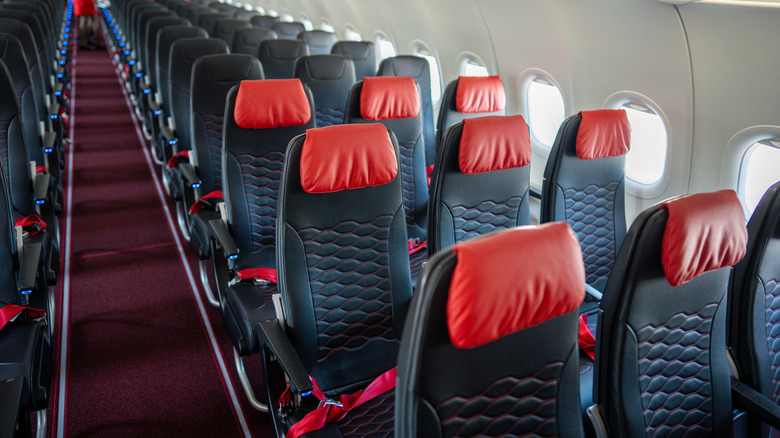 Rows of empty seats with red headrests inside an airplane