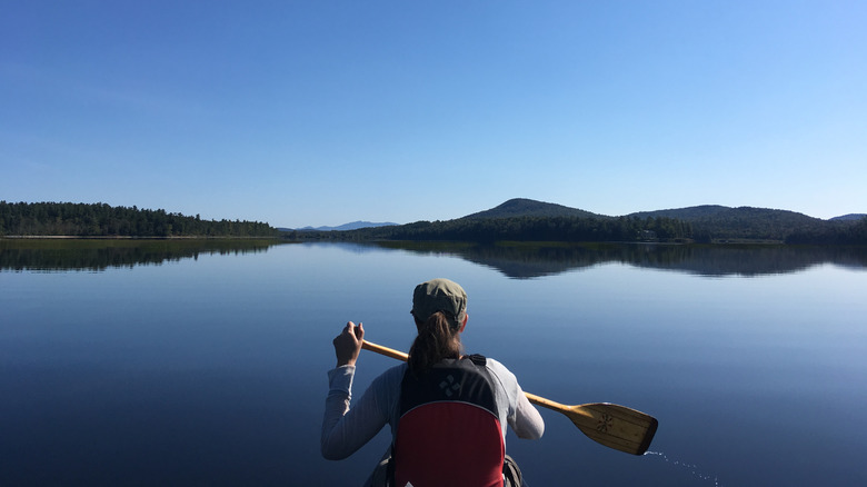 a woman paddles in a lake at adirondacks
