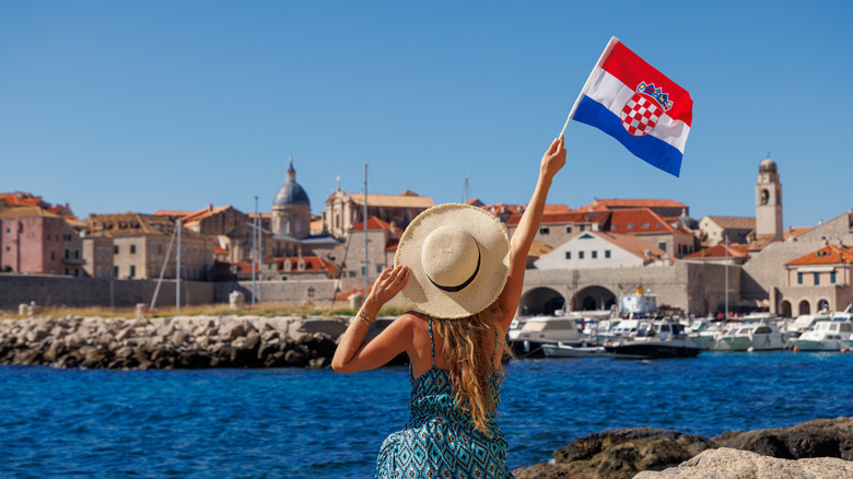 Woman in hat holding Croatian flag near coastal medieval city