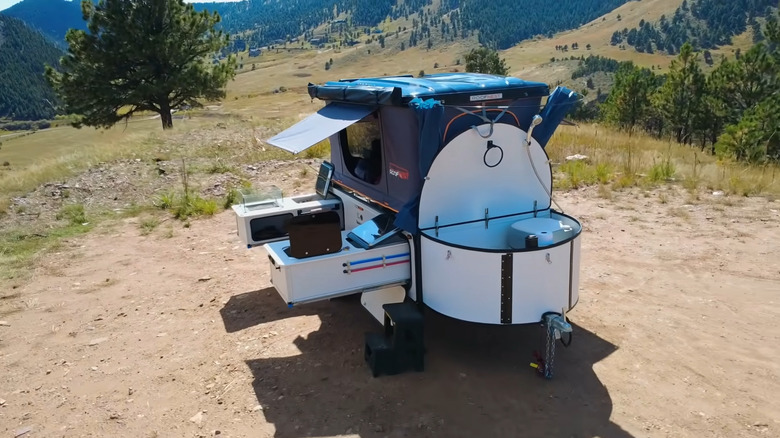 Compact camper trailer with a rooftop tent surrounded by hills