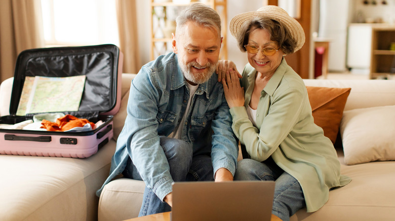 A senior couple in a hotel room with an open suitcase looking excitedly at a laptop