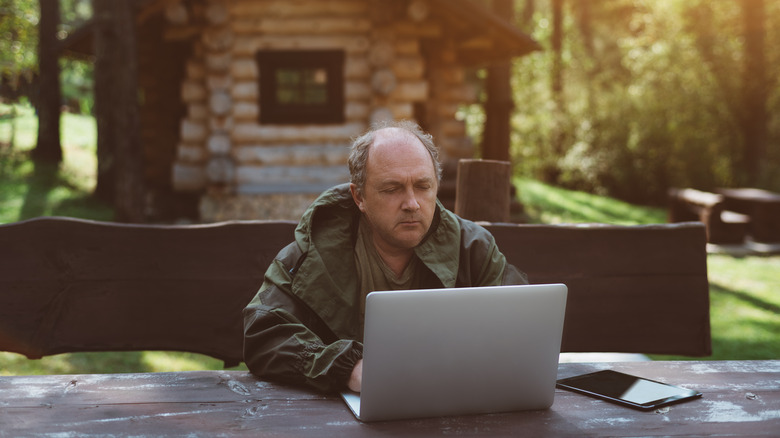 Man using laptop computer on a table outside hunting cabin