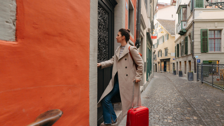 A woman with a red suitcase opening the door to a building