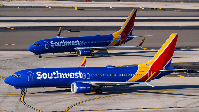 Two Southwest Airlines planes that are blue with yellow and red tails, sitting on tarmac
