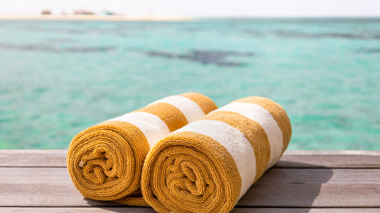 Two rolled-up towels lie on wood planks in front of turquoise waters