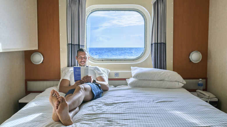Man lying in cruise ship cabin bed reading a book