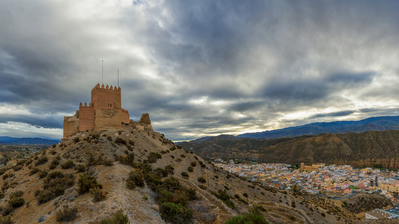 Small medieval castle on desert hill overlooking town and mountains of Tabernas