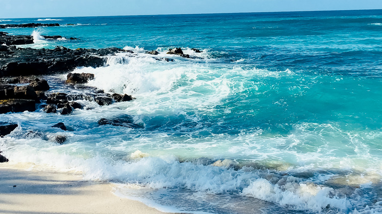Waves crashing on the black lava rocks on the shore at Manini'owali Beach in Hawaii