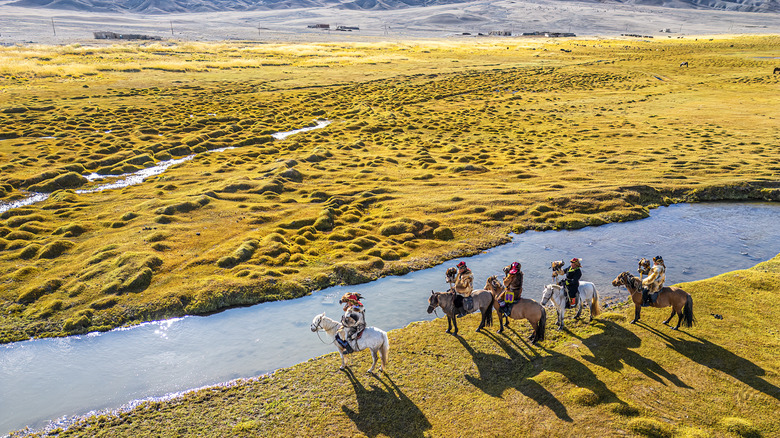 Eagle hunters on horsebacks by a stream surrounded by green grasslands in Mongolia