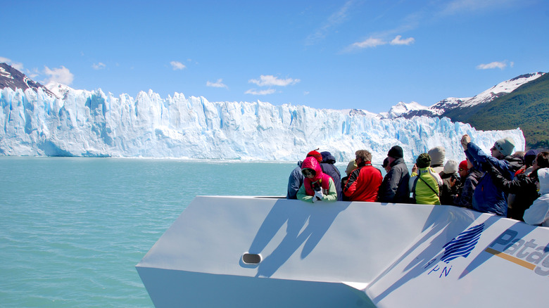 Tourists on the deck of a cruise liner admiring a gigantic glacier ahead of them