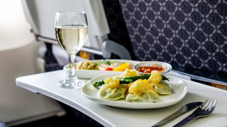 A glass of white wine and plate of food served on an airplane tray table