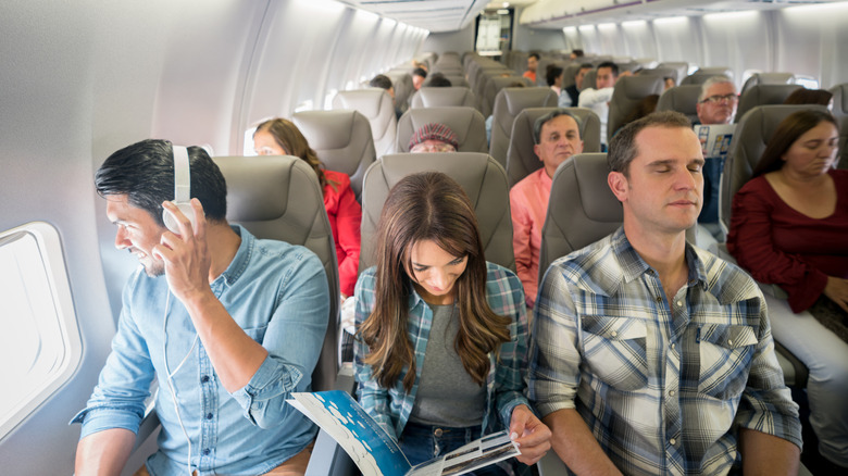 A woman sitting between two men in an airplane row.