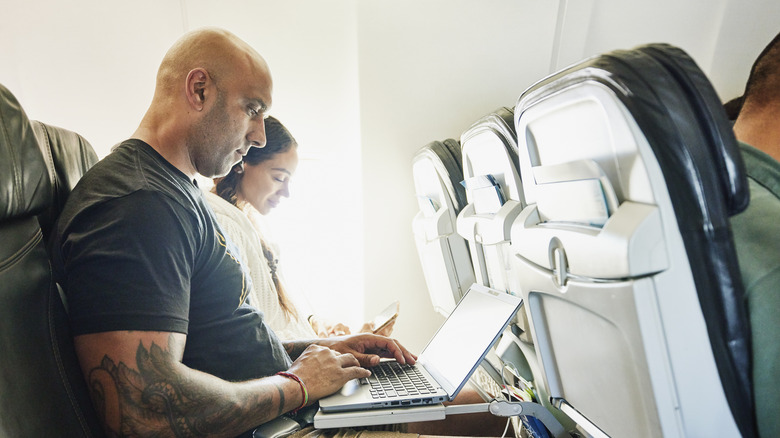 A man in the middle seat working on his laptop.