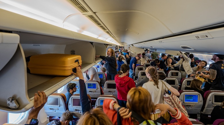 A full plane with people putting bags in the overhead bins.