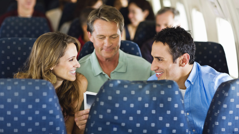 A man calmly reading between two other airline passengers
