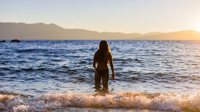 Woman standing in waves of Lake Tahoe beach at sunset