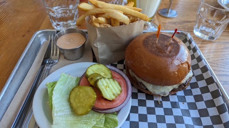 Burger with plate of condiments and fries at Cassell's Hamburgers