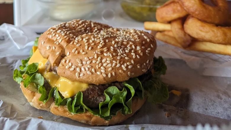 Burger with sesame bun and onion rings in background from My Brother's Bar