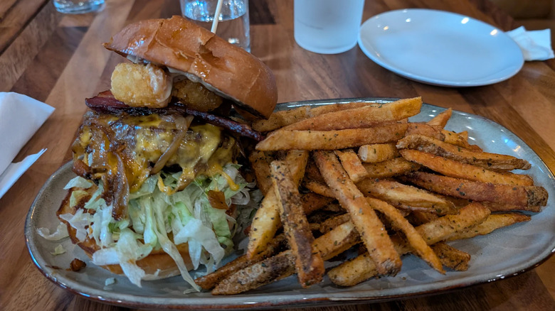 Large burger with tots, sauteed onions, cheese, bacon, and lettuce, and fries from the Farmer & the Cow