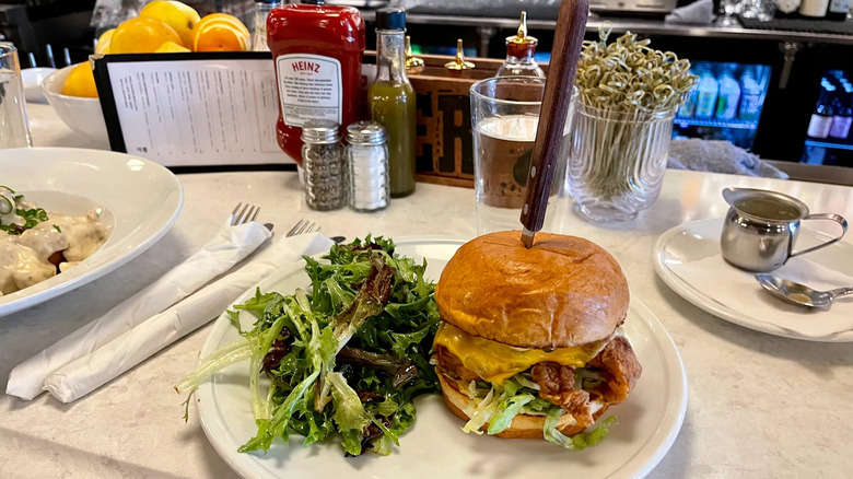 Bacon cheeseburger with knife sticking out of the bun, side salad, and condiments at Pullman Bar