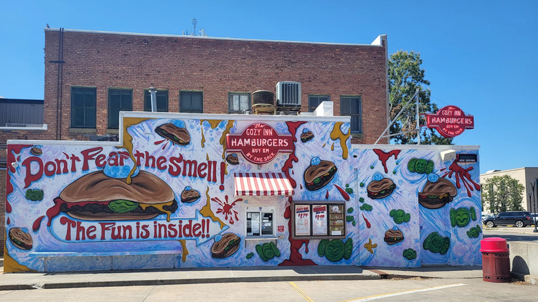 Exterior of the Cozy Inn, with a large mural of burgers that says "Don't fear the smell! the fun is inside!!"