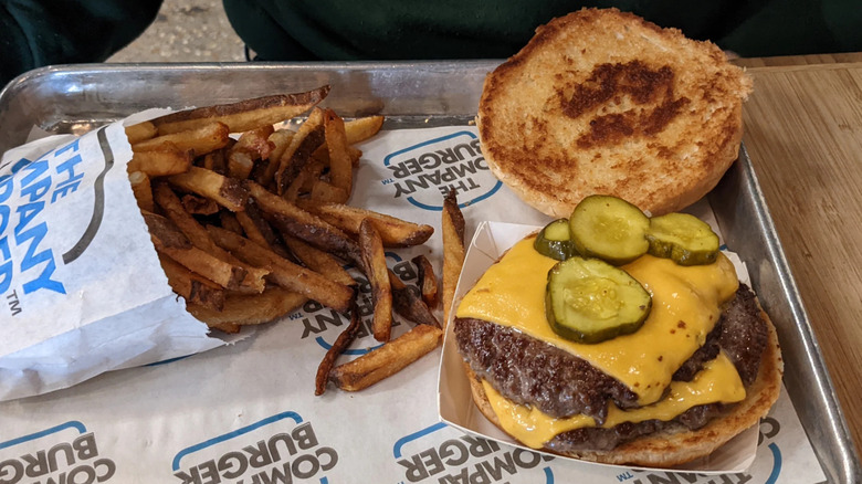 Double cheeseburger with pickles and side of fries on tray from the Company Burger