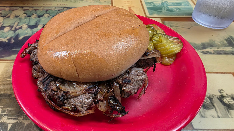 Onion burger with pickles on side on red plate from Sid's Diner