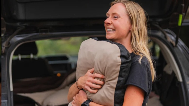 A woman holding a Luno Packable Camping Pillow in front of an SUV hatch set up for sleeping