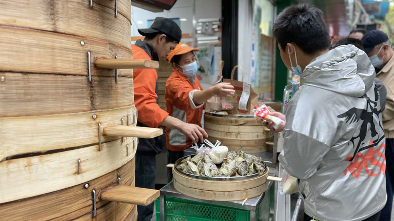 Locals buying steamed streetfood in the morning from a kiosk, bamboo steamers in the foreground