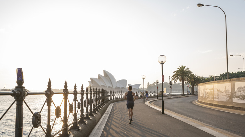 A jogger running toward Sydney Opera House in early morning sunlight