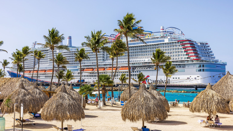 Carnival Cruise Line ship docked in Curacao near a beach with palm trees and thatched cabanas