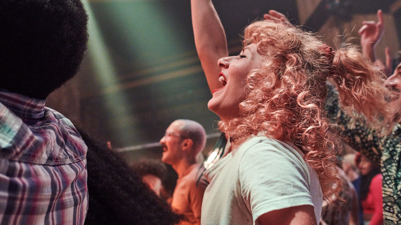 Crowd of young adults watching a concert, with a focus on a young woman with curly hair