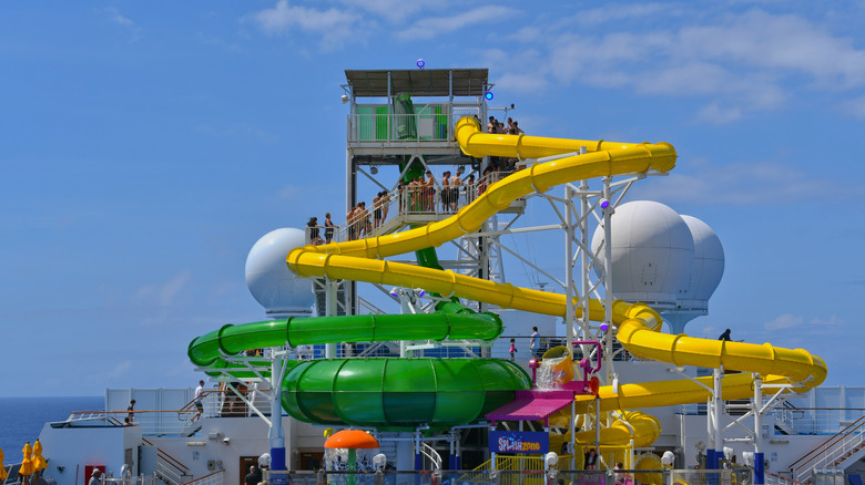 Green and yellow winding watertubes of waterslides on the top deck of a ship, backdrop of sea
