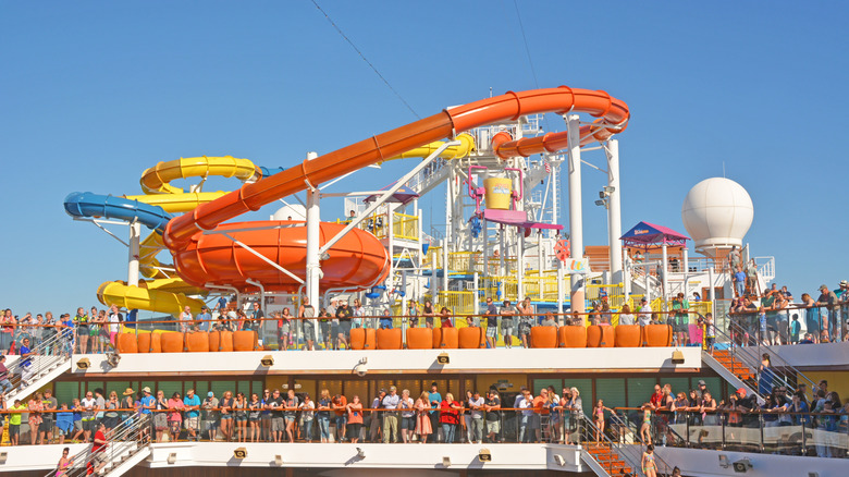 Massive orange and yellow water slide tubes on a crowded top deck of a cruise liner