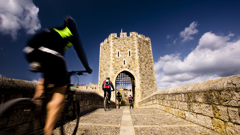 Cyclists crossing a medieval bridge in Besalu, Spain