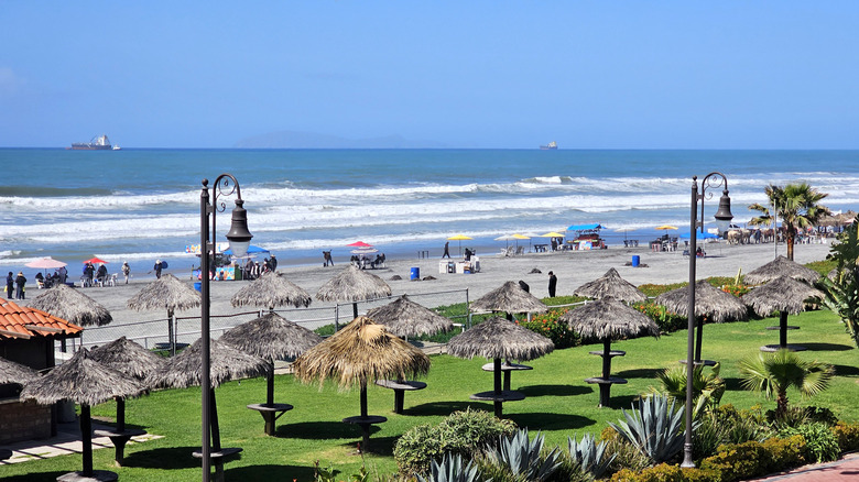 A view of Rosarito Beach in Baja California, Mexico, with white sands and picnic tables under thatch roof umbrellas