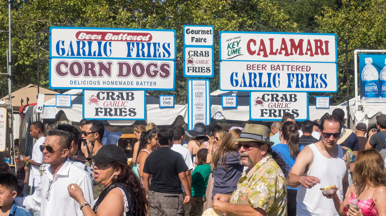 People walking around under large signs denoting different foods at the Gilroy Garlic Festival