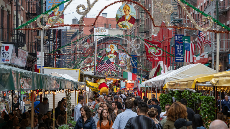 People walking on a crowded street filled with side walk eateries and colorful banners at the Feast of San Gennaro in Little Italy, New York City