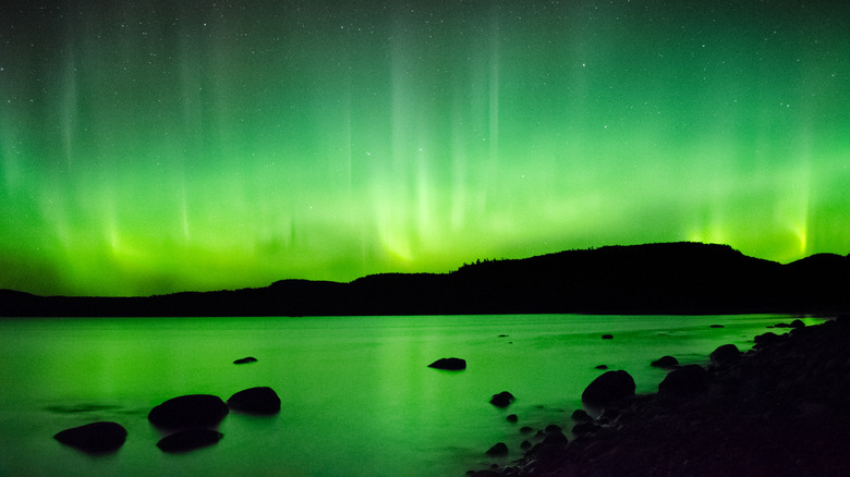 Green lights of the aurora borealis rising above Lake Superior and a rocky shoreline