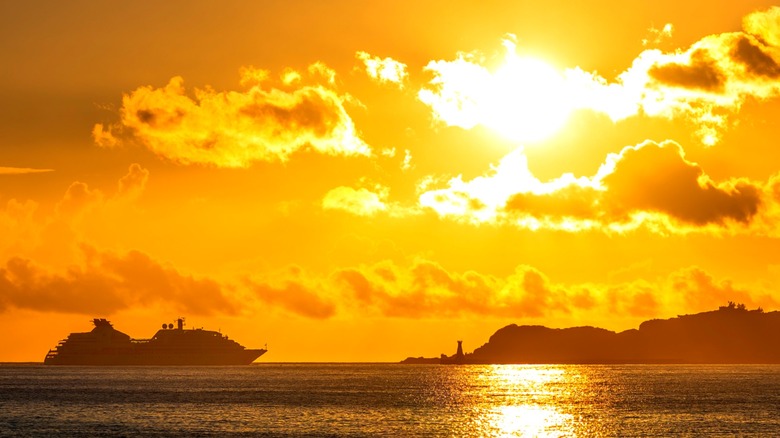 A cruise ship approaching port, silhouetted by a bright sunset