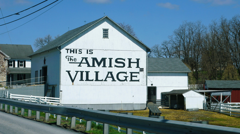A white barn with text on it that reads "This Is The Amish Village"