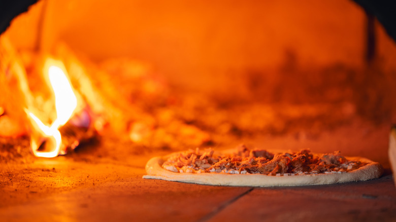 Authentic pizza baking in wood-fired oven with glowing flame and crispy crust