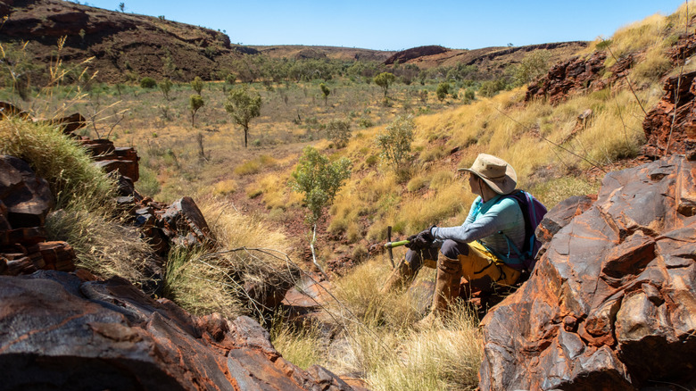 A woman sitting leaning against the rocks in a desert landscape, rockhammer in hand