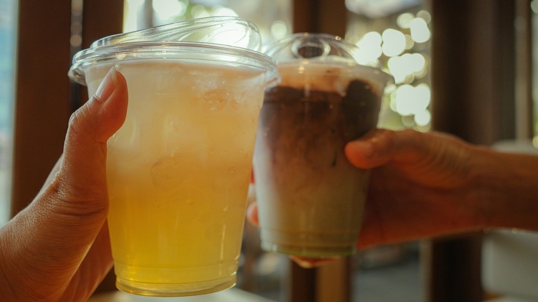 Two hands toasting with dirty sodas in plastic cups