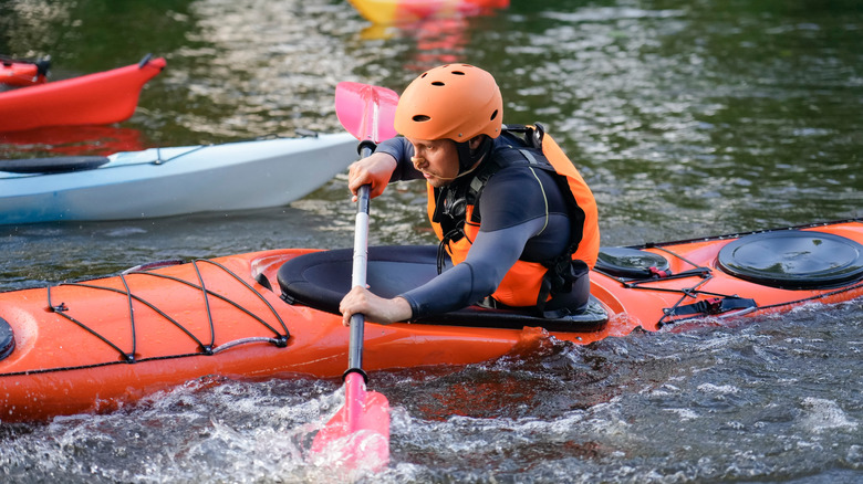 Man with a helmet and life jacket kayaking on a river