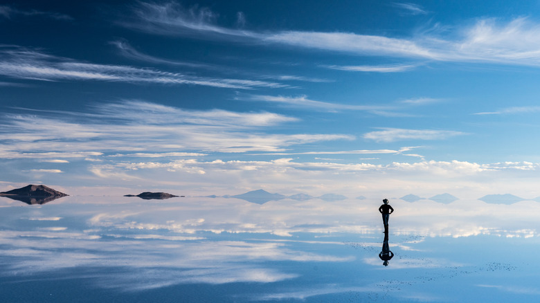 Person standing on Bolivia's salt flats reflected in the watery sands