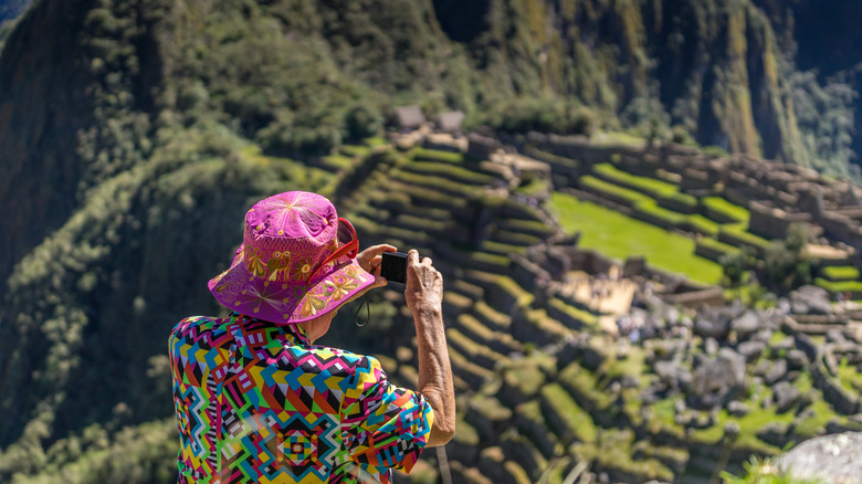 Older man in colorful clothes taking pictures of Machu Picchu, Peru
