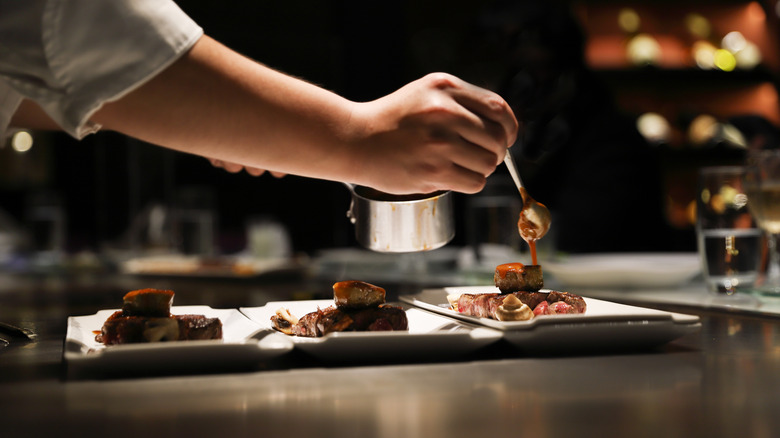 Chef adding sauce to steak plates in kitchen